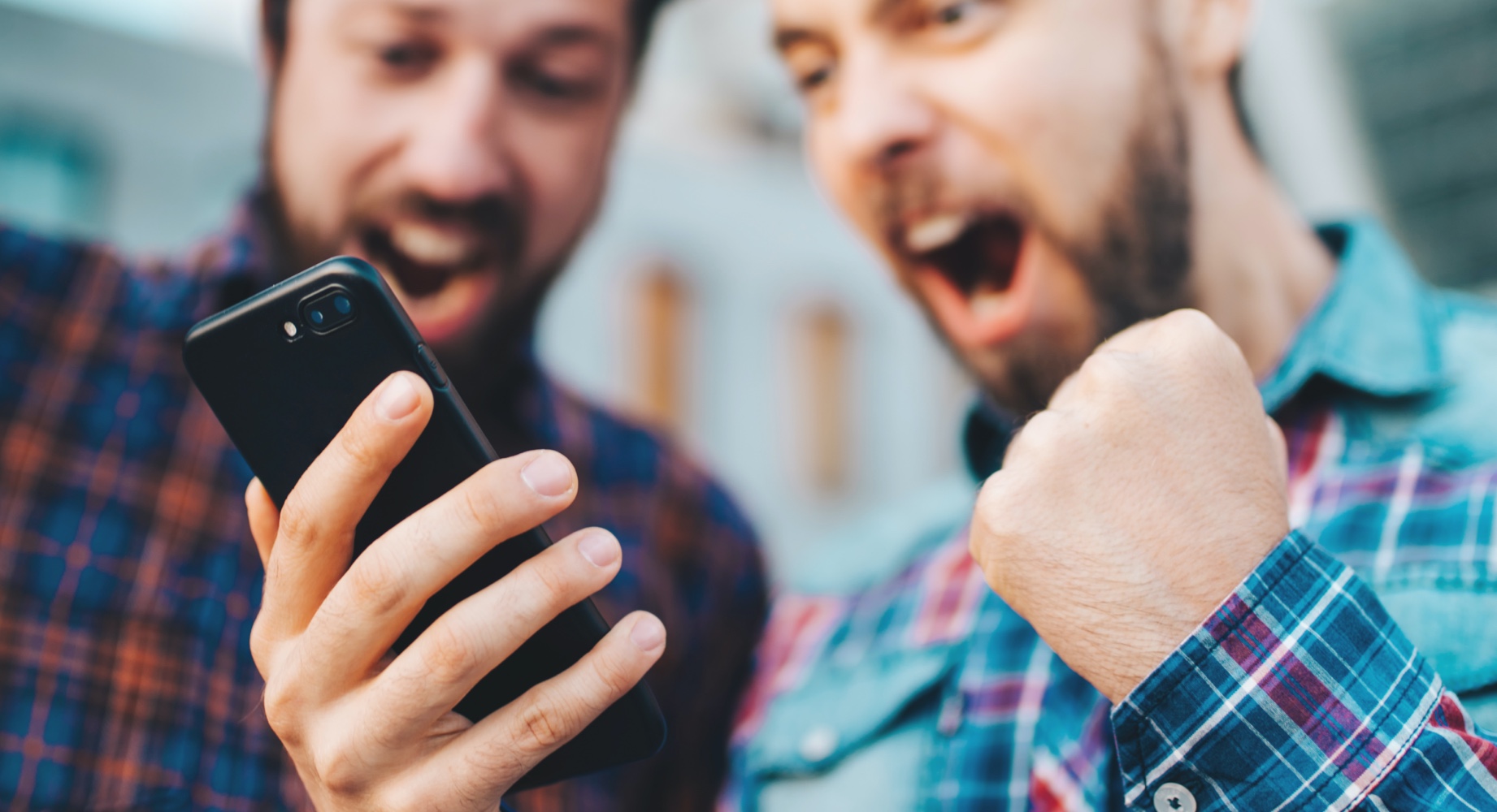 Two men celebrating while looking at a smartphone, one clenching his fist