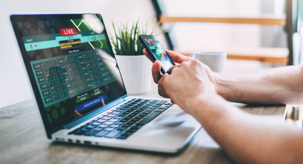 Man betting on mobile with scoreboard on laptop