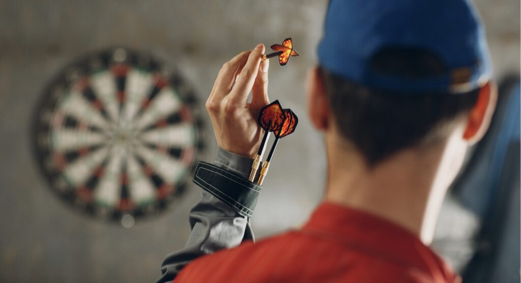 Man throwing aiming at dartboard with two darts strapped around wrist