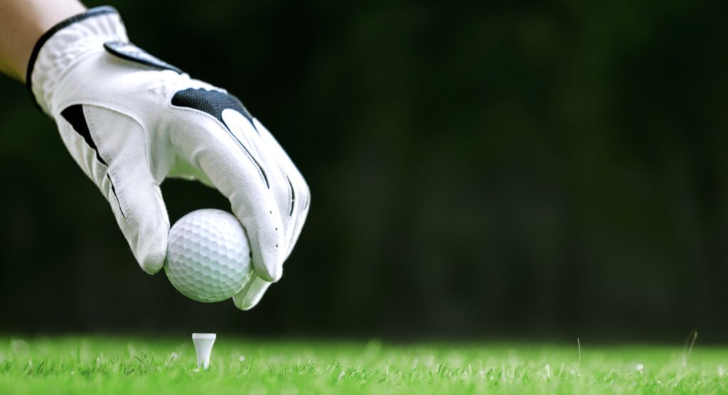 Golfer placing ball on tee with gloved hand