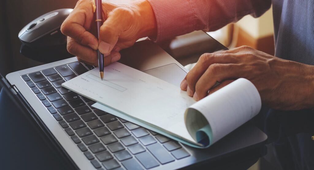 Man writing cheque on open laptop