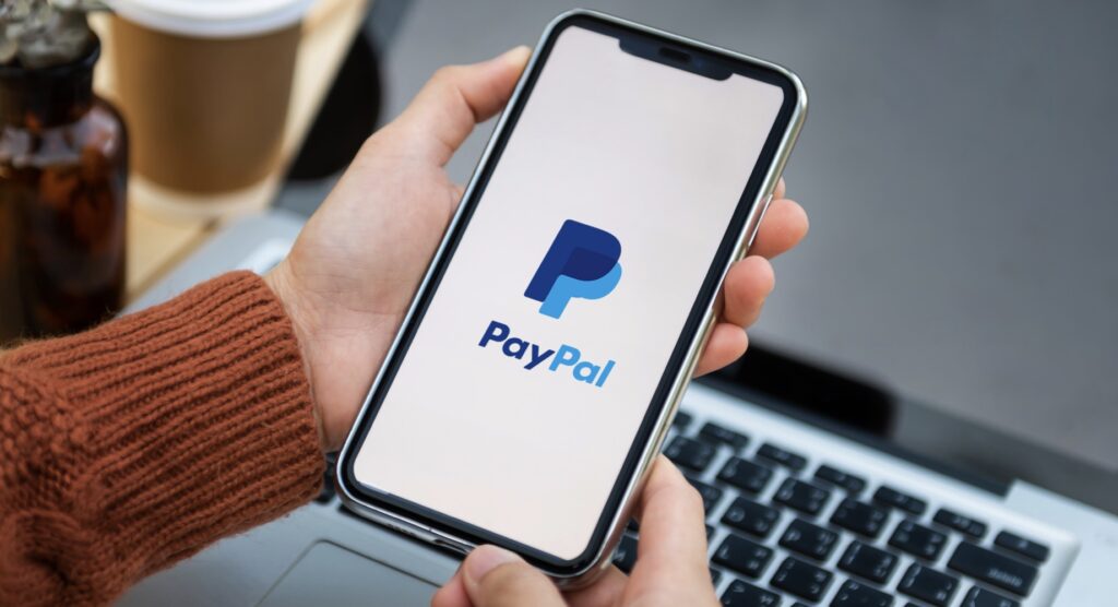 Person holding a smartphone with PayPal logo on screen Person holding a smartphone with PayPal logo on screen