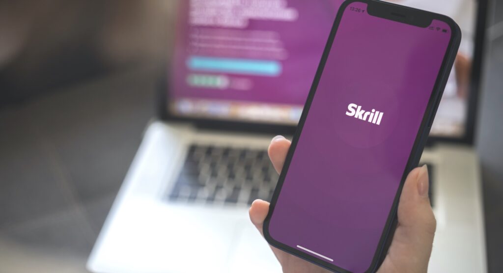 Female holding smartphone displaying Skrill logo