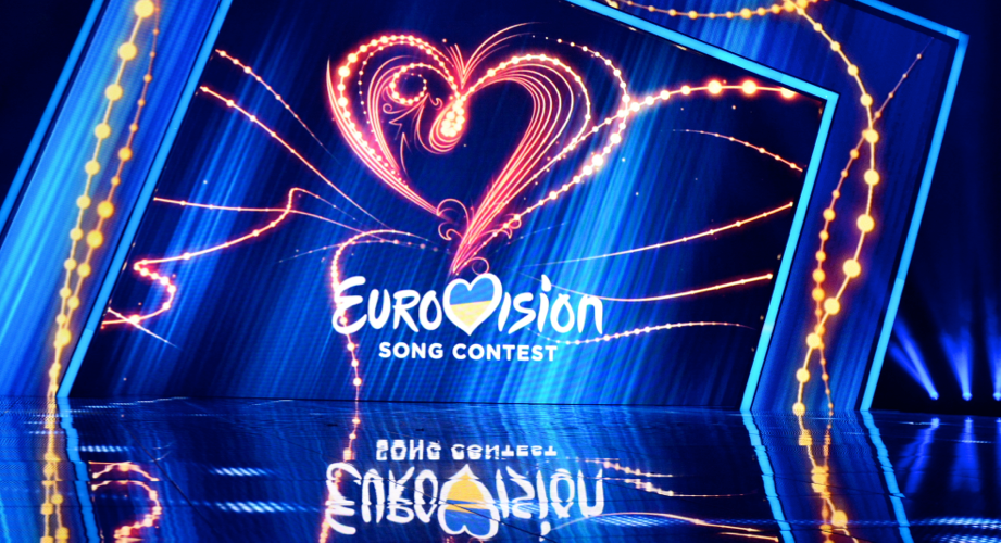 A vibrantly lit stage with a heart and the Eurovision Song Content logo projected onto the background. 