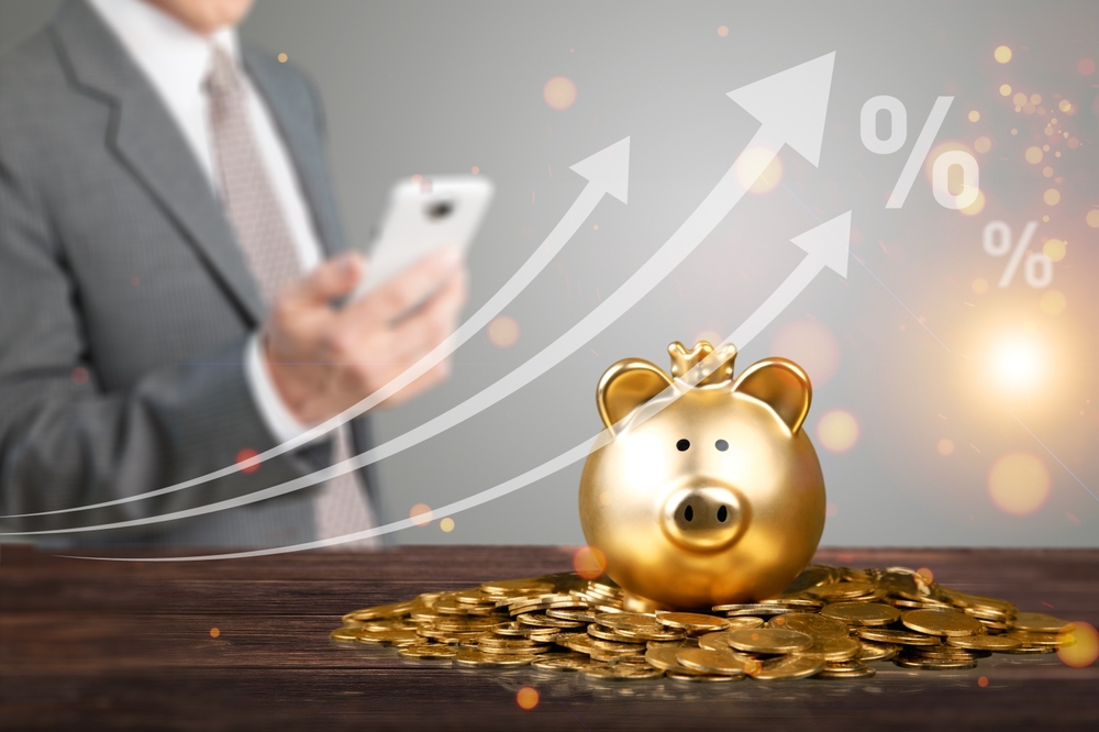 Gold piggy bank on coins with rising arrows and percentage symbols Gold piggy bank wearing a crown on a pile of coins, with rising arrows and percentage symbols overlaid