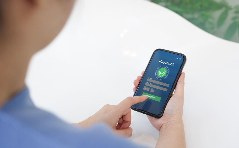 Confirming a secure payment on a smartphone Person tapping Confirm on a smartphone payment screen with a security shield icon