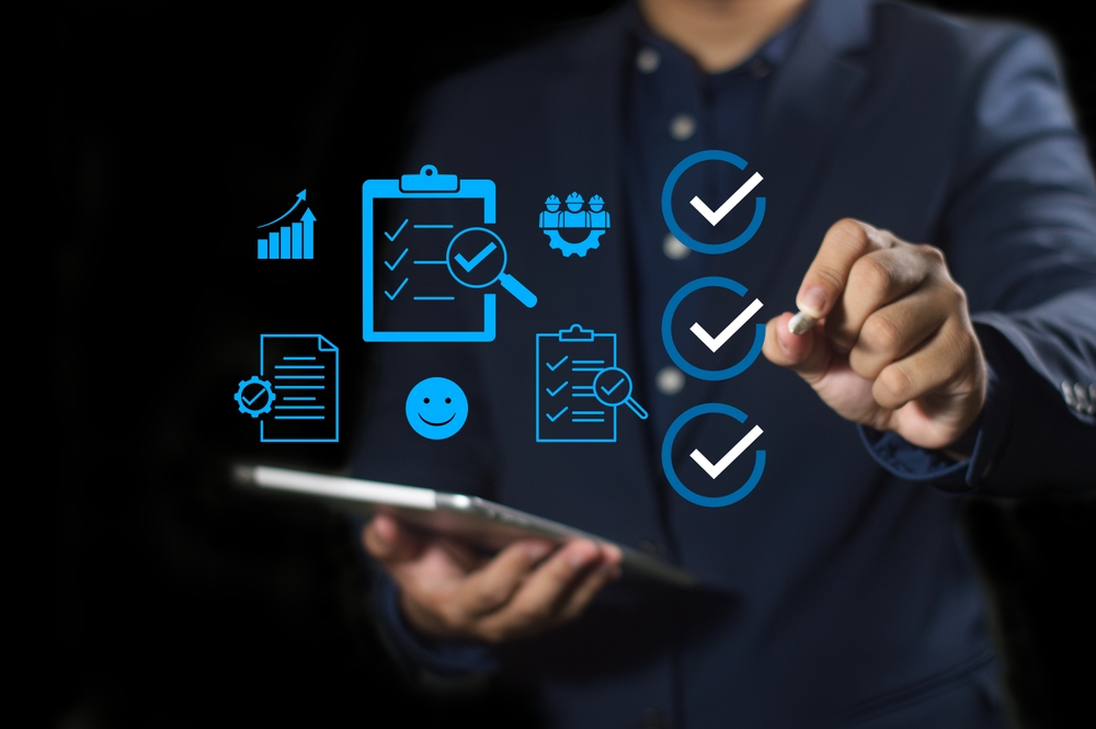 Businessman with digital checklist and quality-check icons Person in a suit holding a tablet with blue checklist and tick mark icons overlaid