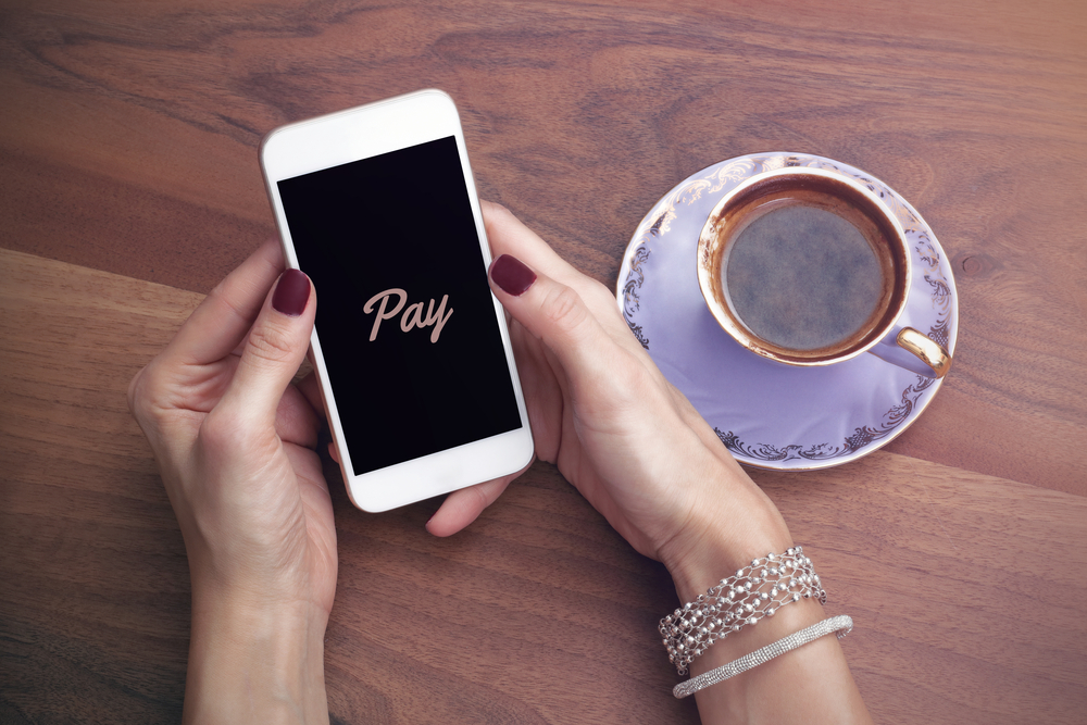 Mobile payment on a smartphone Hands holding a smartphone displaying the word Pay, beside a cup of coffee on a wooden table