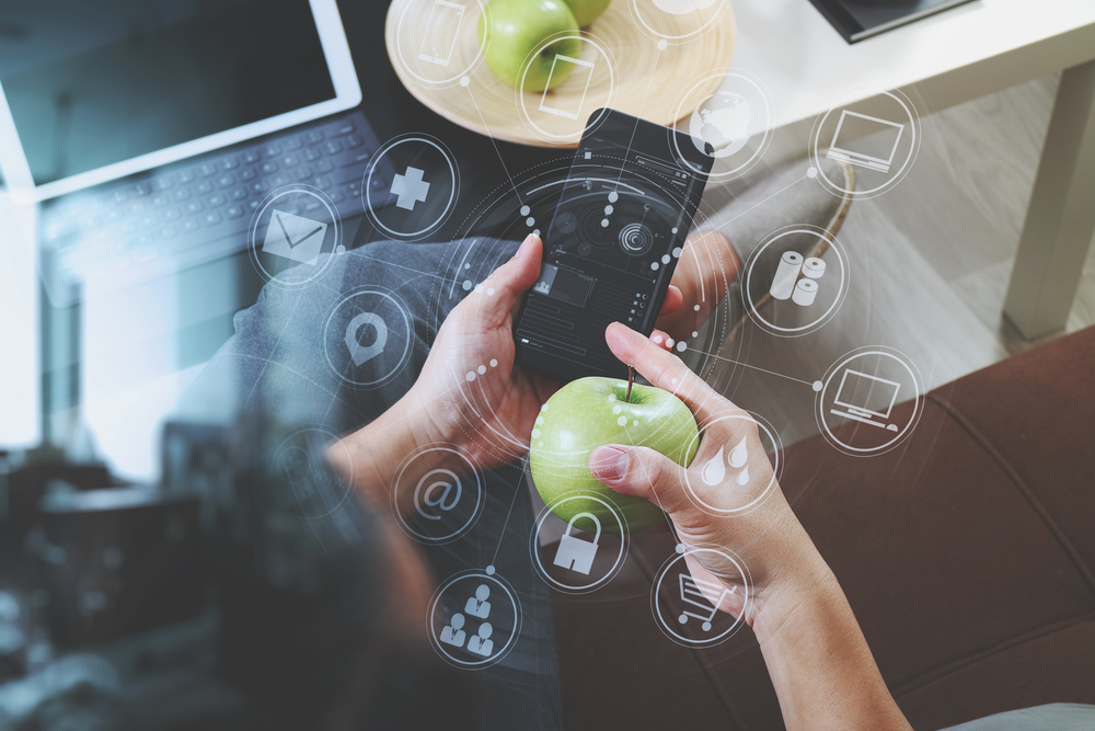 Smartphone and apple with digital connectivity icons Hands holding a smartphone and a green apple, with digital technology icons overlaid