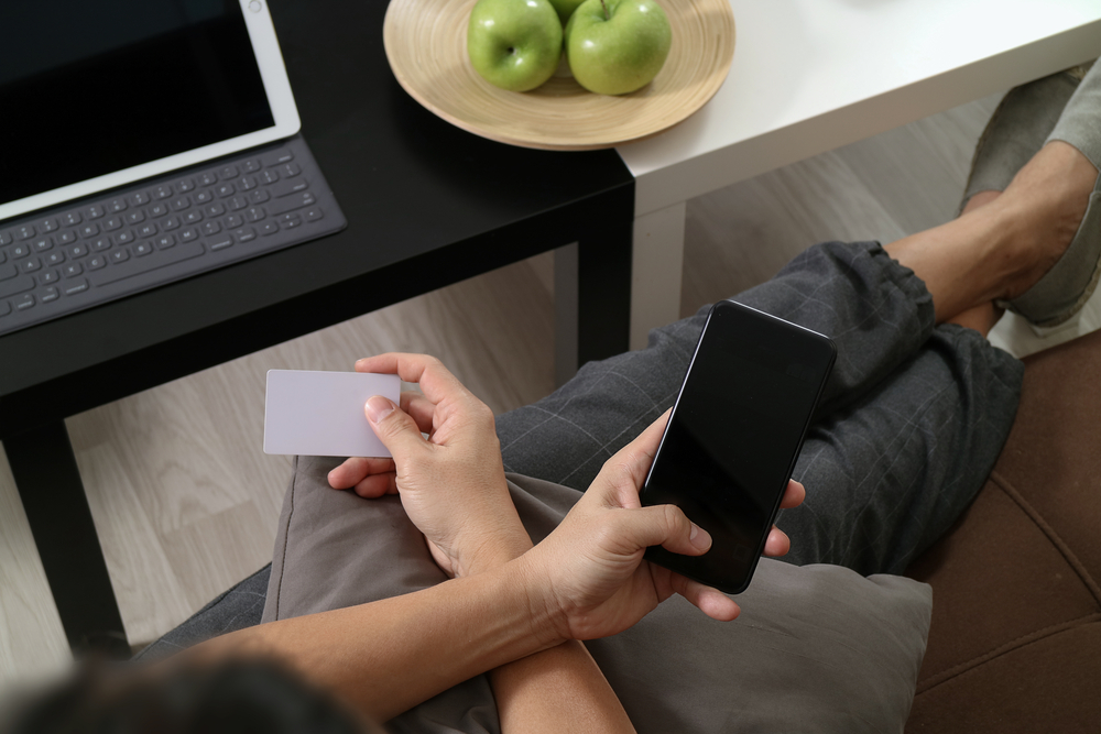 Making a mobile payment with a card and smartphone Person holding a blank payment card and a smartphone while sitting at a desk