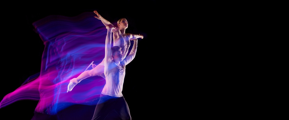 Ice dance pair performing a lift under coloured lights