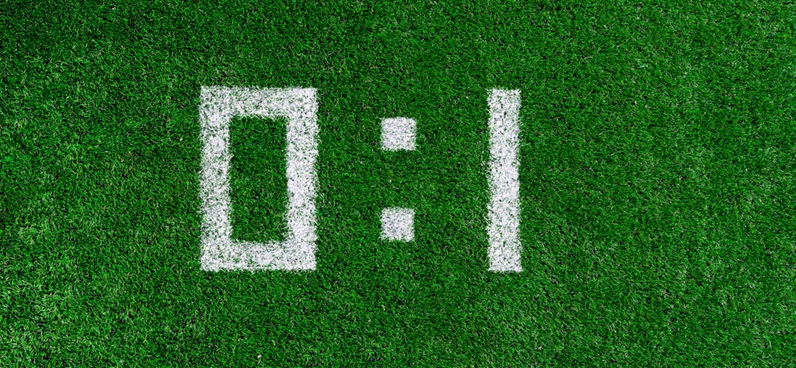 $100 bill and pencil on bet slip White numerals on grass show a score of 0:1
